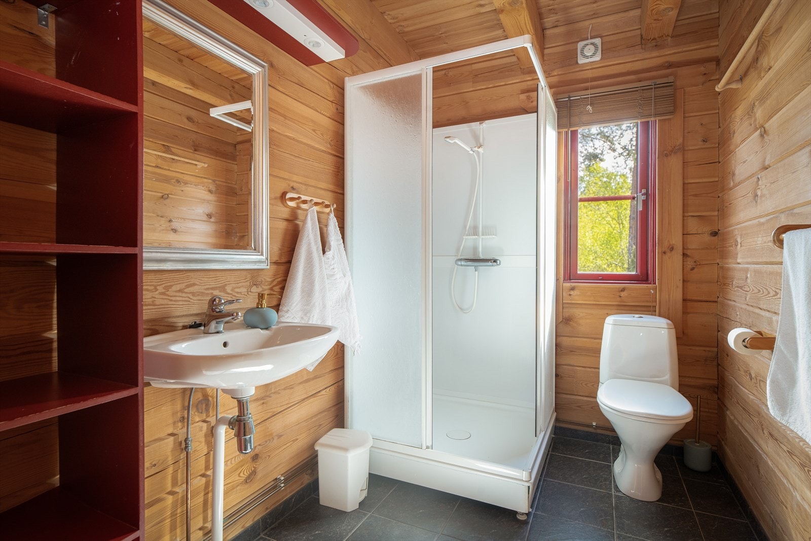 Badet i 1. etasje har adkomst fra stua, med flislagt gulv og tømmervegger som i hytta for øvrig. Badet er innredet med veggmontert servant, dusjkabinett og toalett. Galleribilde