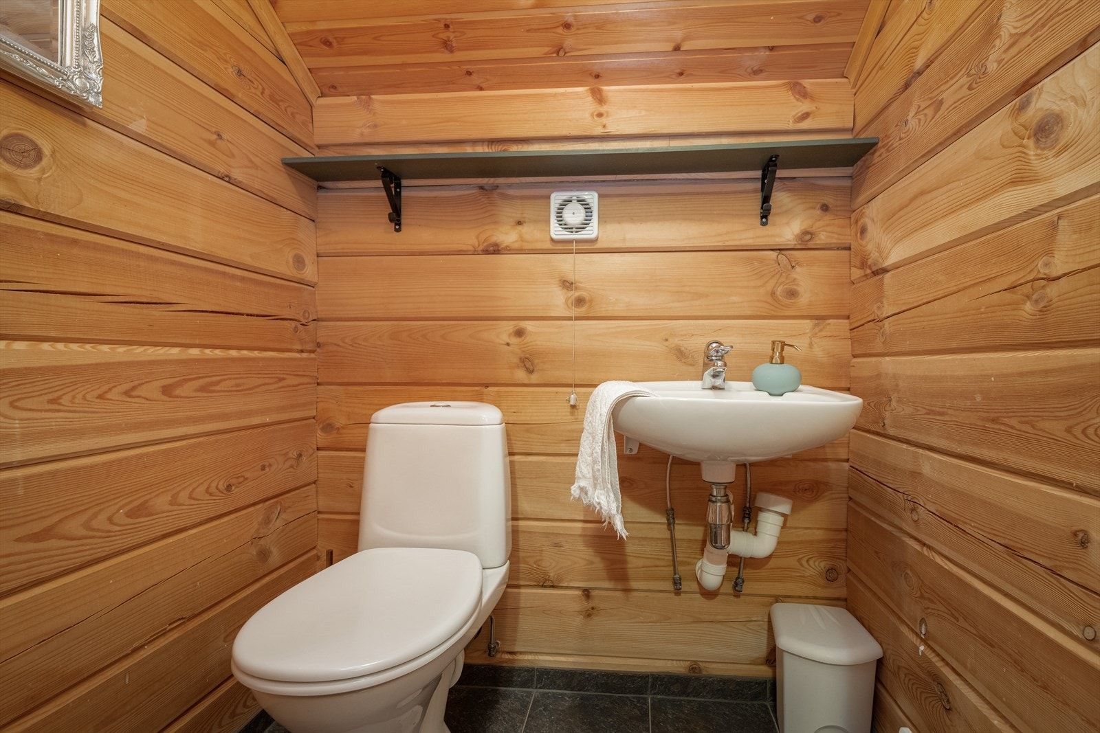 Toalettrommet i 2. etasje har flislagt gulv og tømmer på veggene. Her er det servant med ett-greps batteri og toalett. Galleribilde