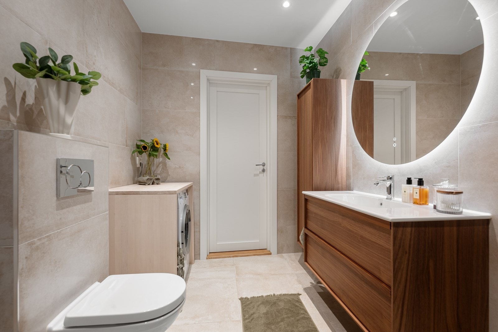 Gulv og vegger er belagt med store fliser (ca. 60 x 60 cm) - Badet har innredning med skap og servantbenk i valnøtt, stort speil med integrert belysning og antiduggfunksjon samt stikkontakt plassert i skuffinnredning Galleribilde