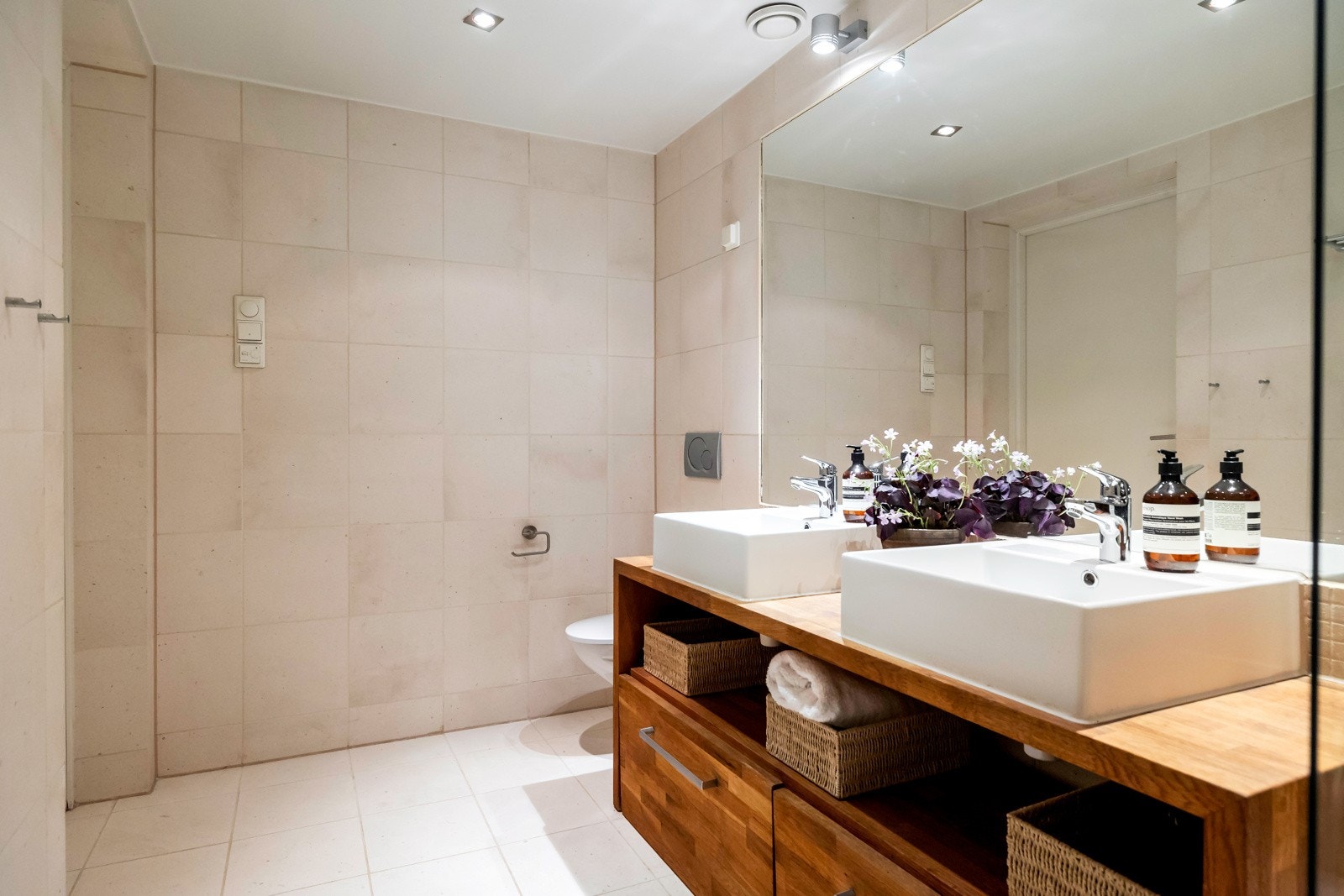 Innredet med to toppmonterte servanter over hylle, skuffer med stort speil og belysning over, innmurt badekar med veggmontert armatur og glassvegg, samt vegghengt toalett Galleribilde