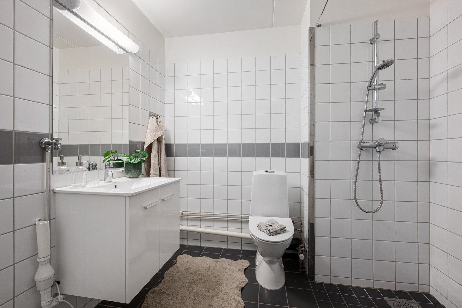 Romslig flislagt bad innredet med servant, speil med lys, toalett og opplegg for vaskemaskin. Galleribilde