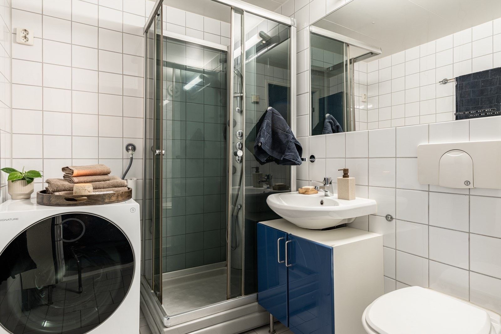 Badet har flislagte overflater, opplegg for vaskemaskin og er innredet med dusjkabinett, vegghengt toalett og servant. Galleribilde