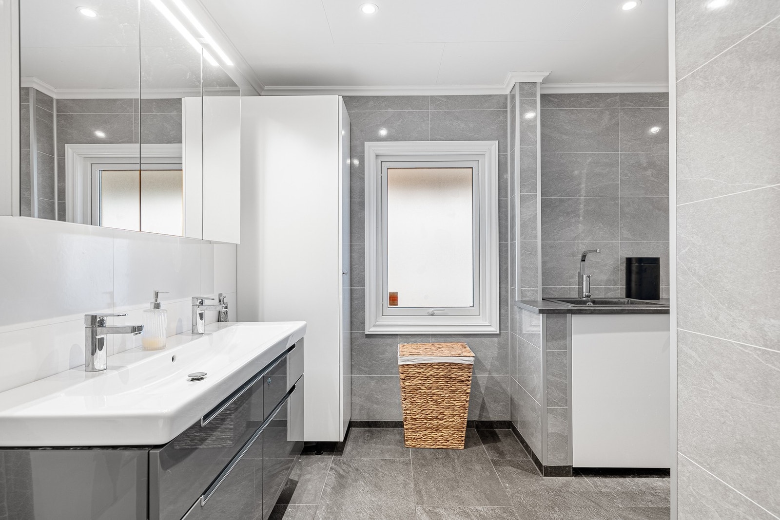 Badet har flislagt gulv med varmekabler, samt baderomsplater og innredning i matchende stil som gir et helhetlig og moderne uttrykk Galleribilde