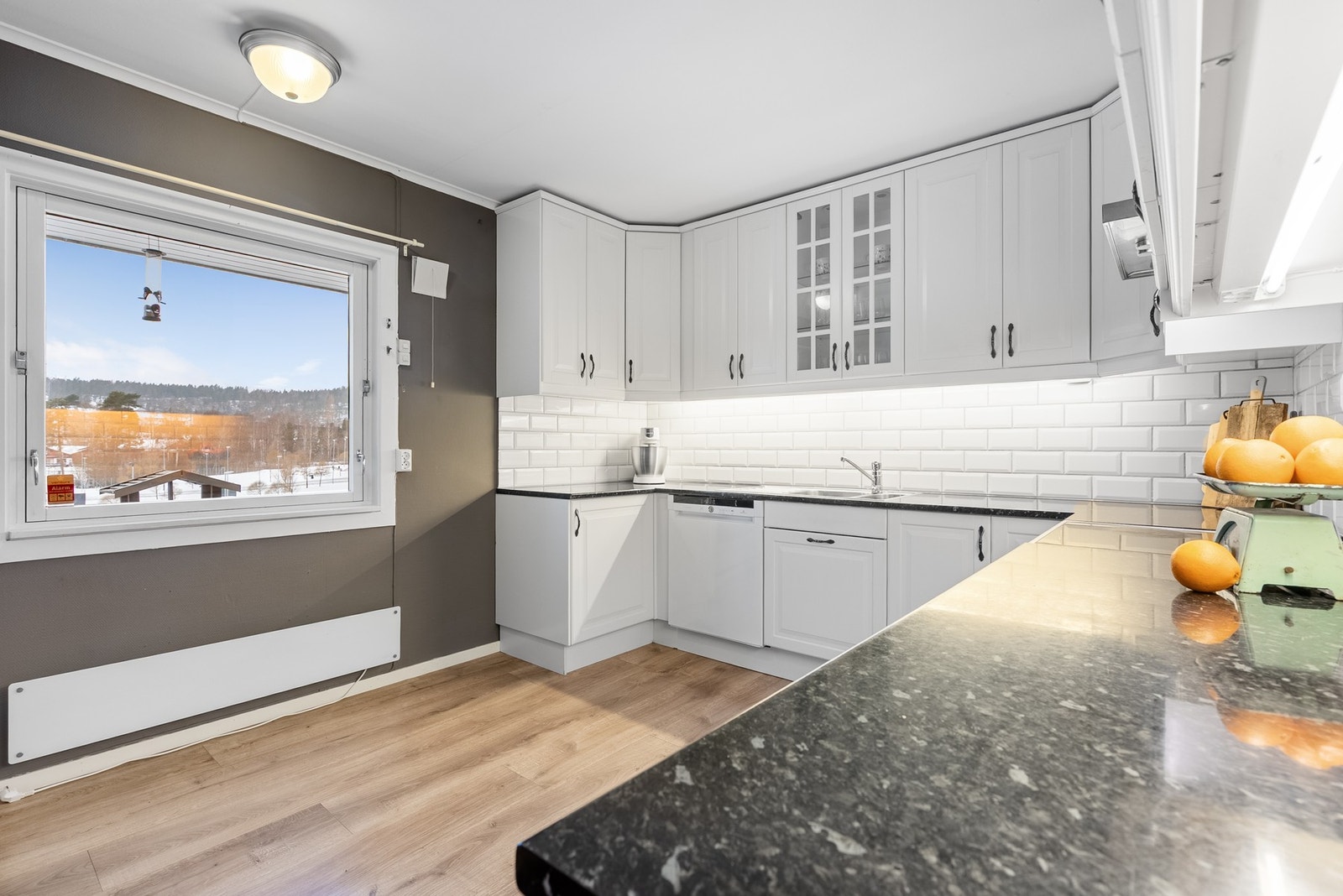 På kjøkkenet har du lyse profilerte fronter med detaljer i vitrineskap - plass til frokostbord ved vinduet og utsyn til Kodal skole Galleribilde