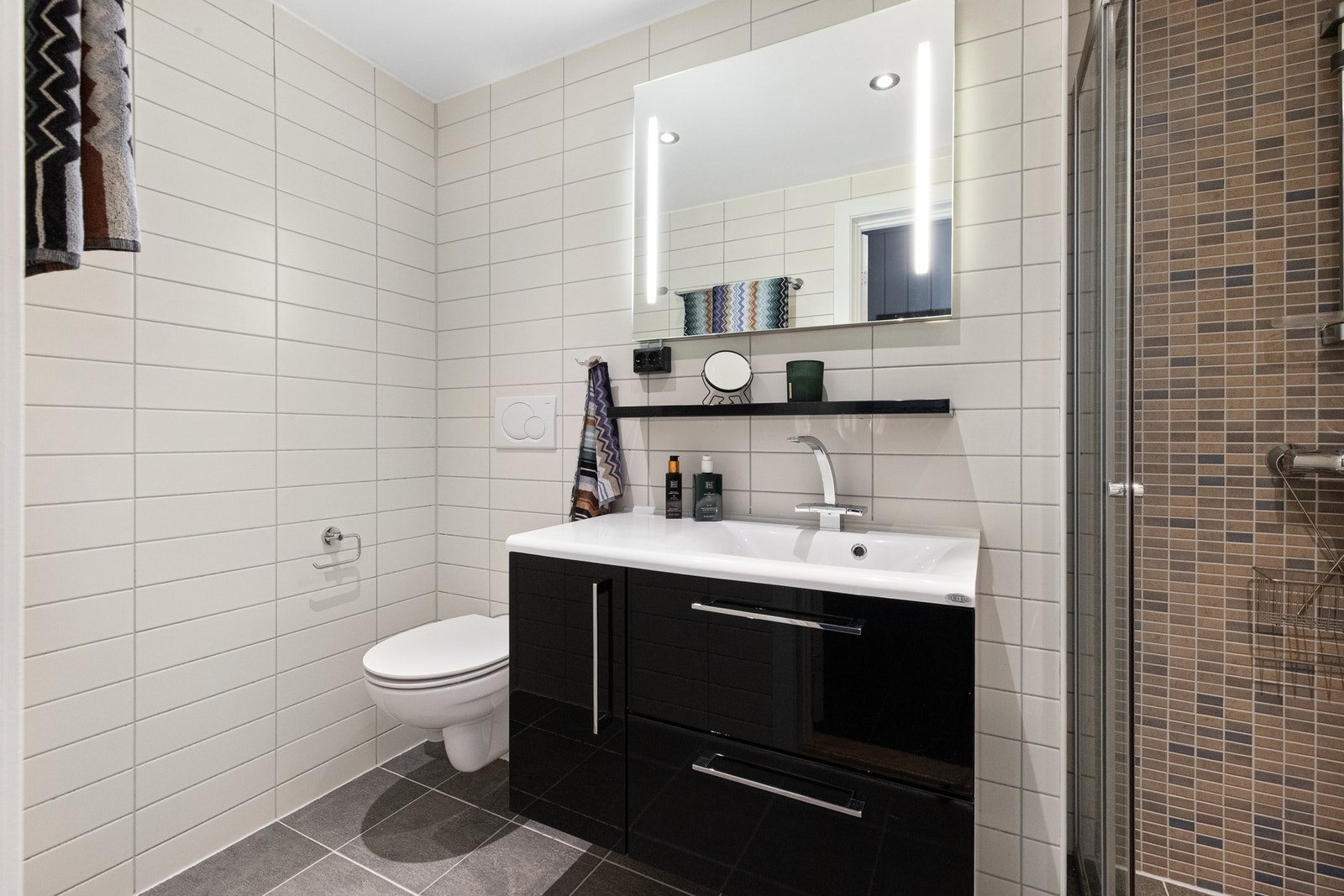 Begge bad har fliser på gulv og vegg. Mørkere mosaikkfliser i dusjnisje Galleribilde