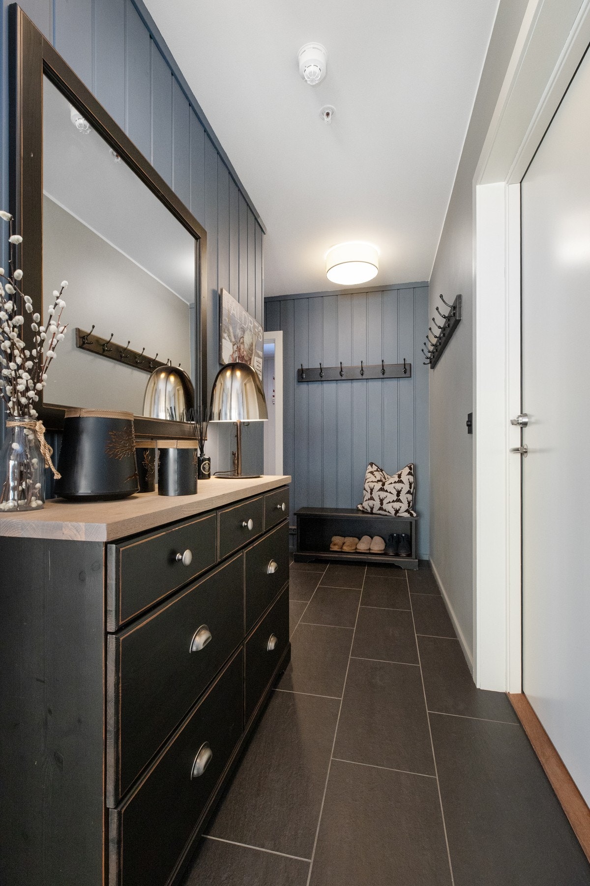 Entré/gang med kvadratisk fliser. Knagger for yttertøy og sittebenk med hylle under Galleribilde