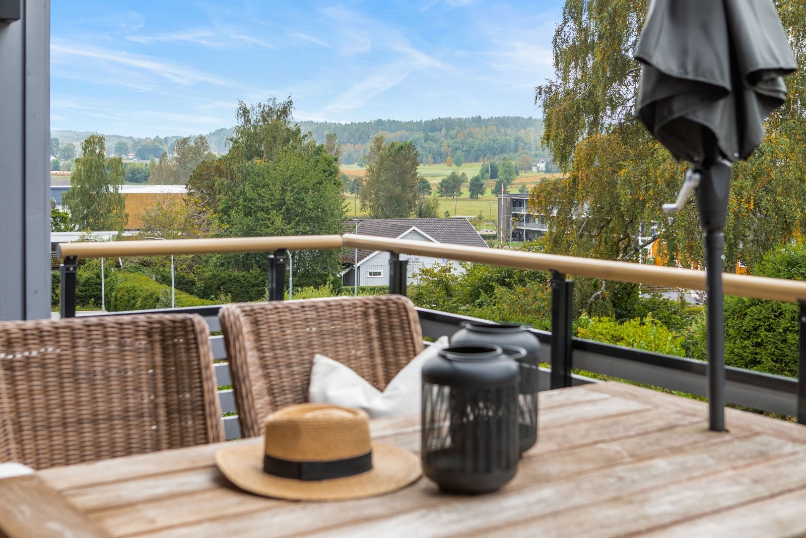 Uteplassen er delvis overbygd og vender ut mot et frodig grøntareal med plen og busker, samt høyreiste trær, prydbusker og skogholt på andre siden av veien. Galleribilde