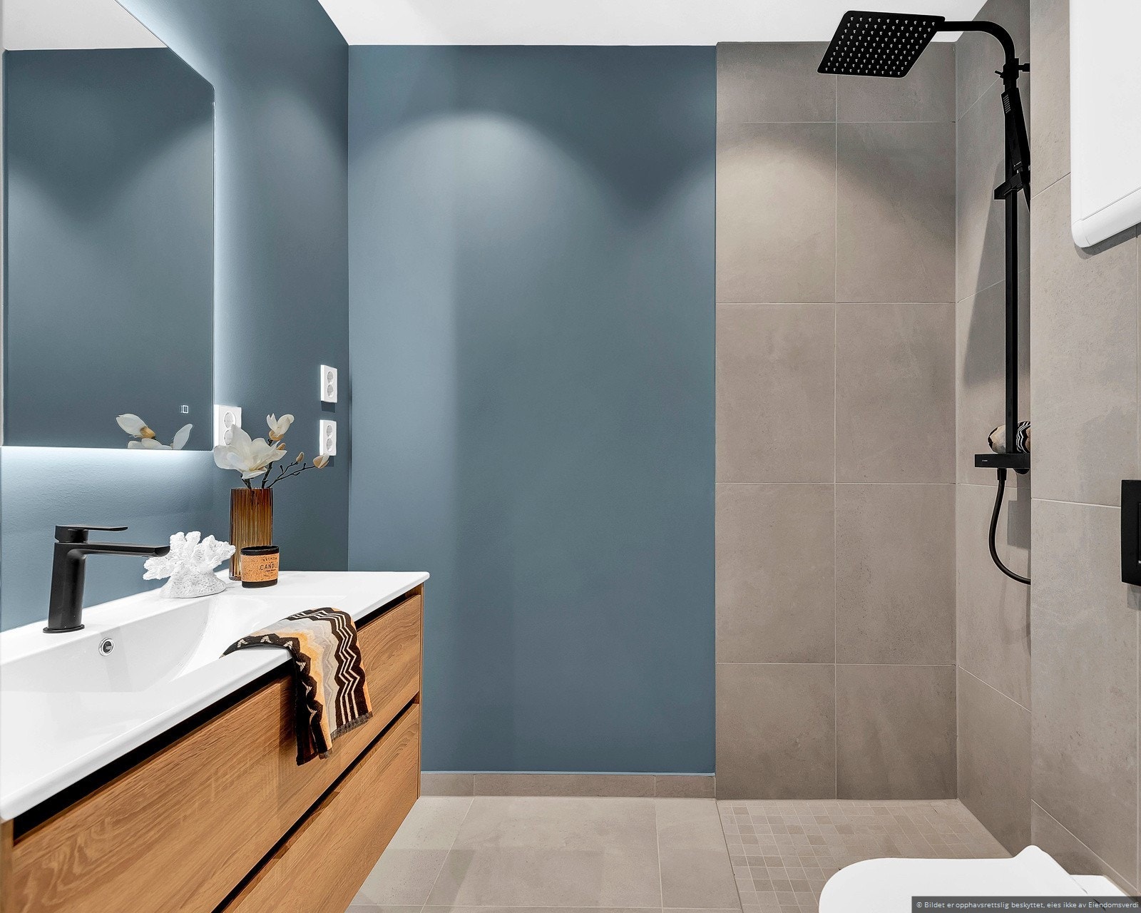 Stilrent baderom, innredet med vegghengt toalett, romslig dusjhjørne og servant med underskap og speil med LED-belysning. Galleribilde