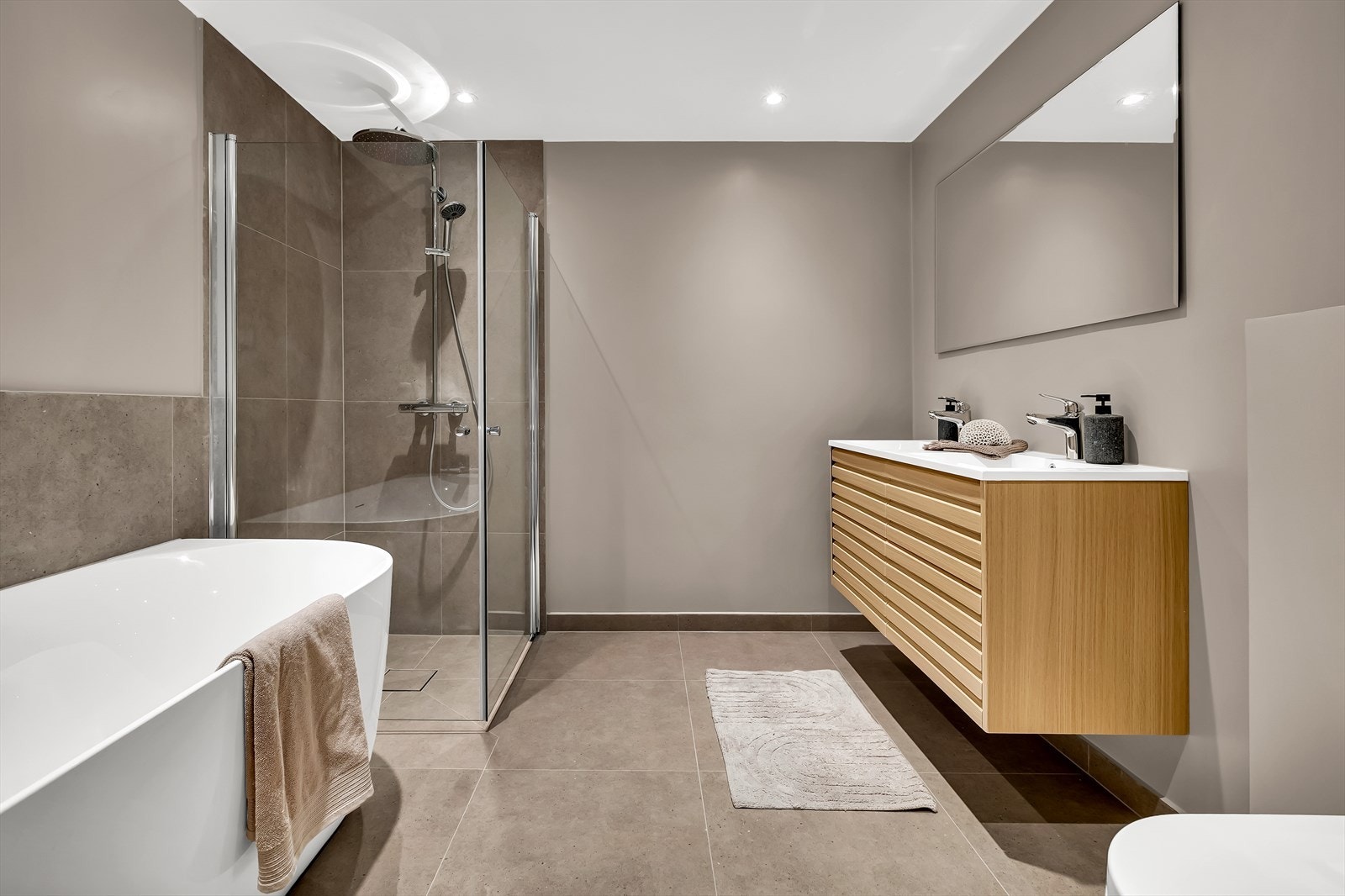 Lekkert bad med dusjhjørne, badekar, dobbelservant med underskap, wc og speil. Galleribilde