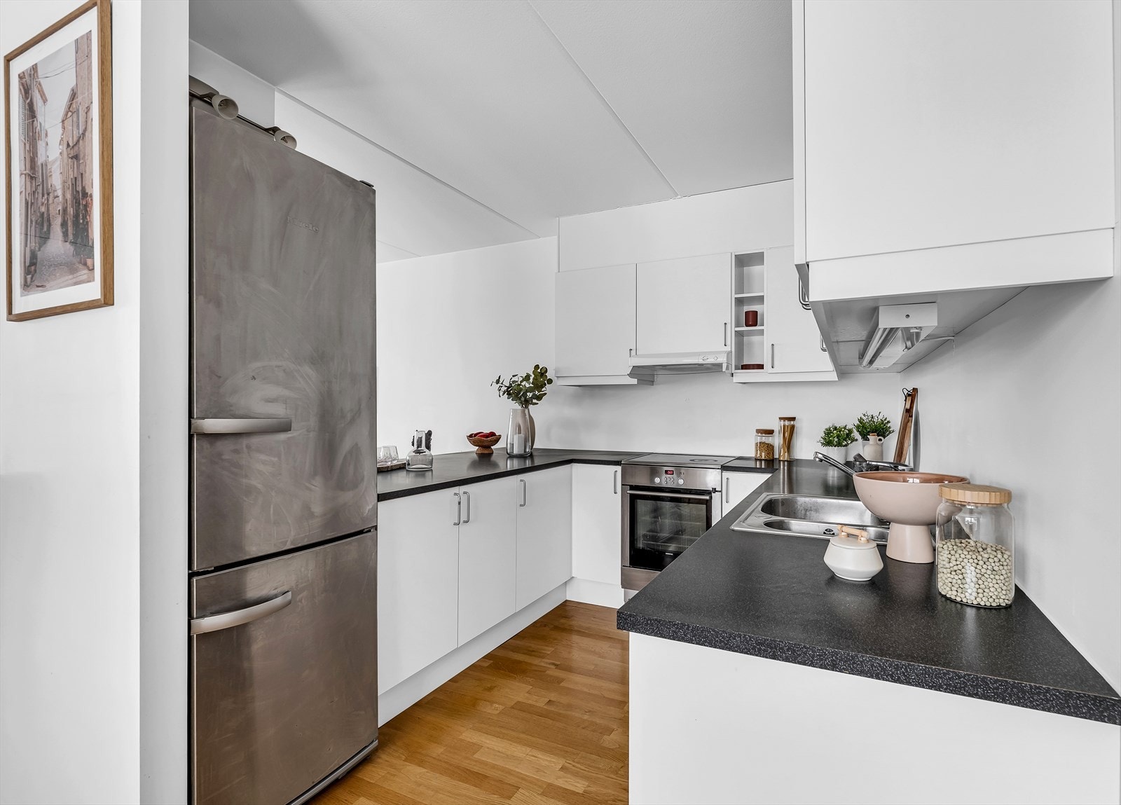 Sigdal kjøkkeninnredning med lyse slette fronter og benkeplate i laminat/finert spon. Kjøkkenet er utstyrt med nedfelt kum i stål, ettgreps blandebatteri og ventilator med integrert avtrekk ut. Galleribilde