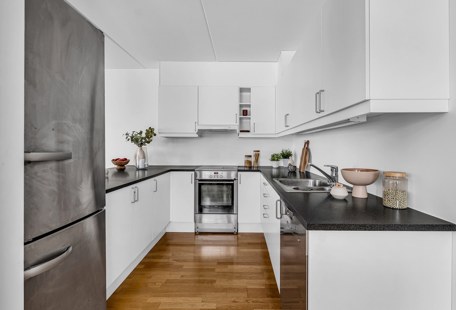 Sigdal kjøkkeninnredning med lyse slette fronter og benkeplate i laminat/finert spon. Kjøkkenet er utstyrt med nedfelt kum i stål, ettgreps blandebatteri og ventilator med integrert avtrekk ut. Galleribilde