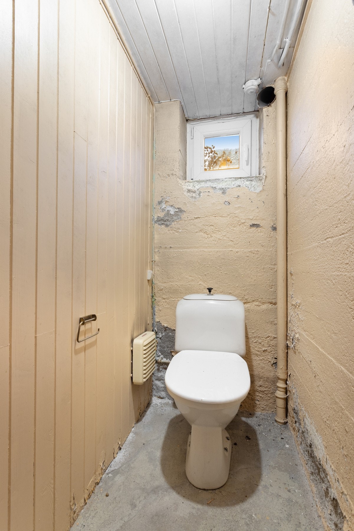 Enkelt toalett rom i kjeller med betong dekke på gulv, malte trepaneler på vegg og i himling. Galleribilde