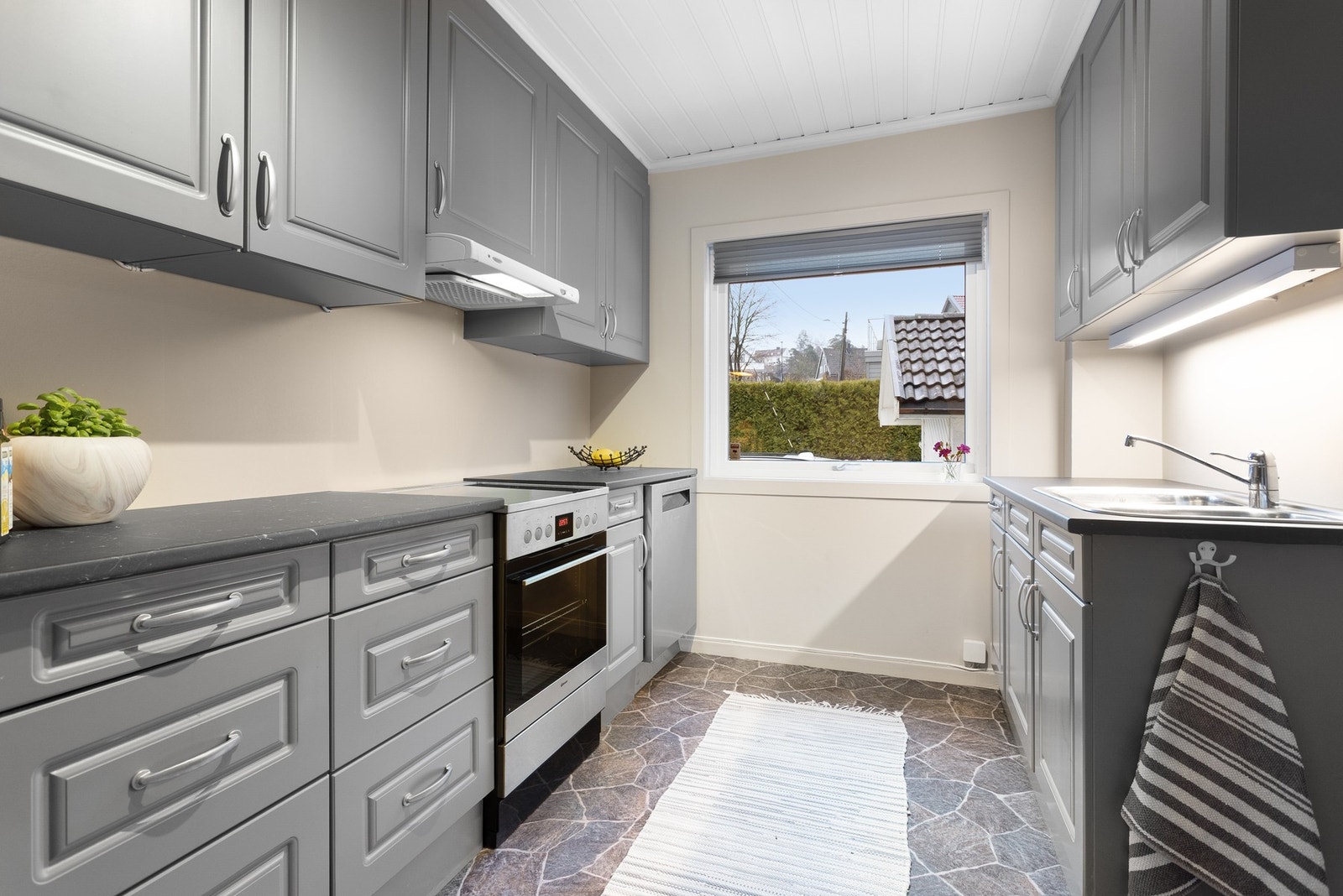 Pent kjøkken med profilerte fronter i lys grå farge og benkeplate i laminat. Galleribilde