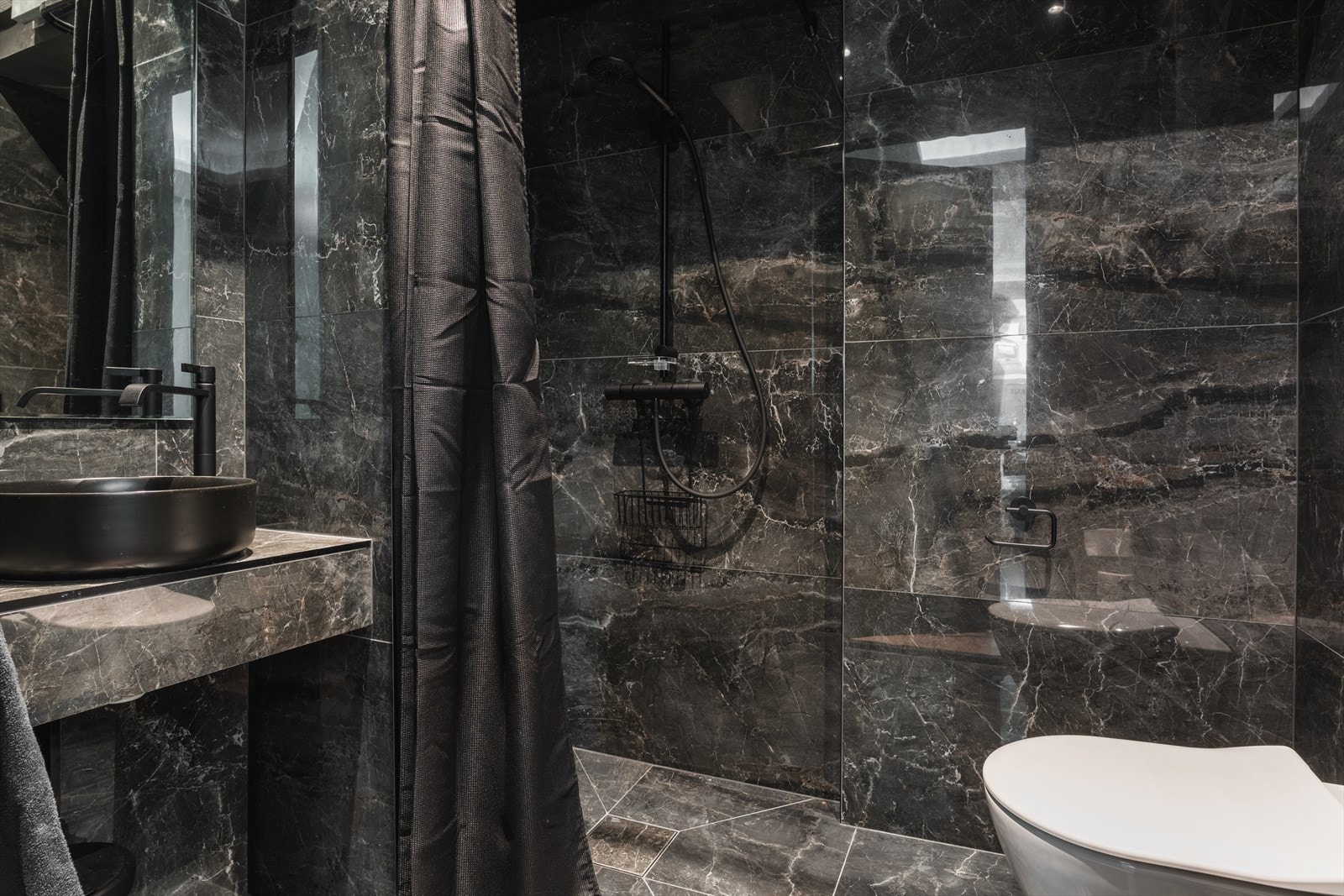 Lekkert flislagt bad utstyrt med servant og speil, toalett og dusjhjørne. Galleribilde