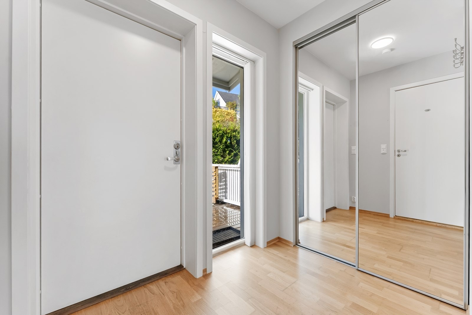 Inn ytterdøren ligger en romslig entré med lyse overflater, parkettgulv og integrert skyvedørsgarderobe med speilfronter. Galleribilde