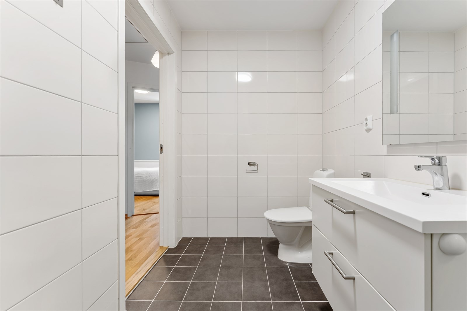 Badet har toalett, servant nedfelt i skuffeseksjon, speil med integrert belysning og dusjsone. Galleribilde