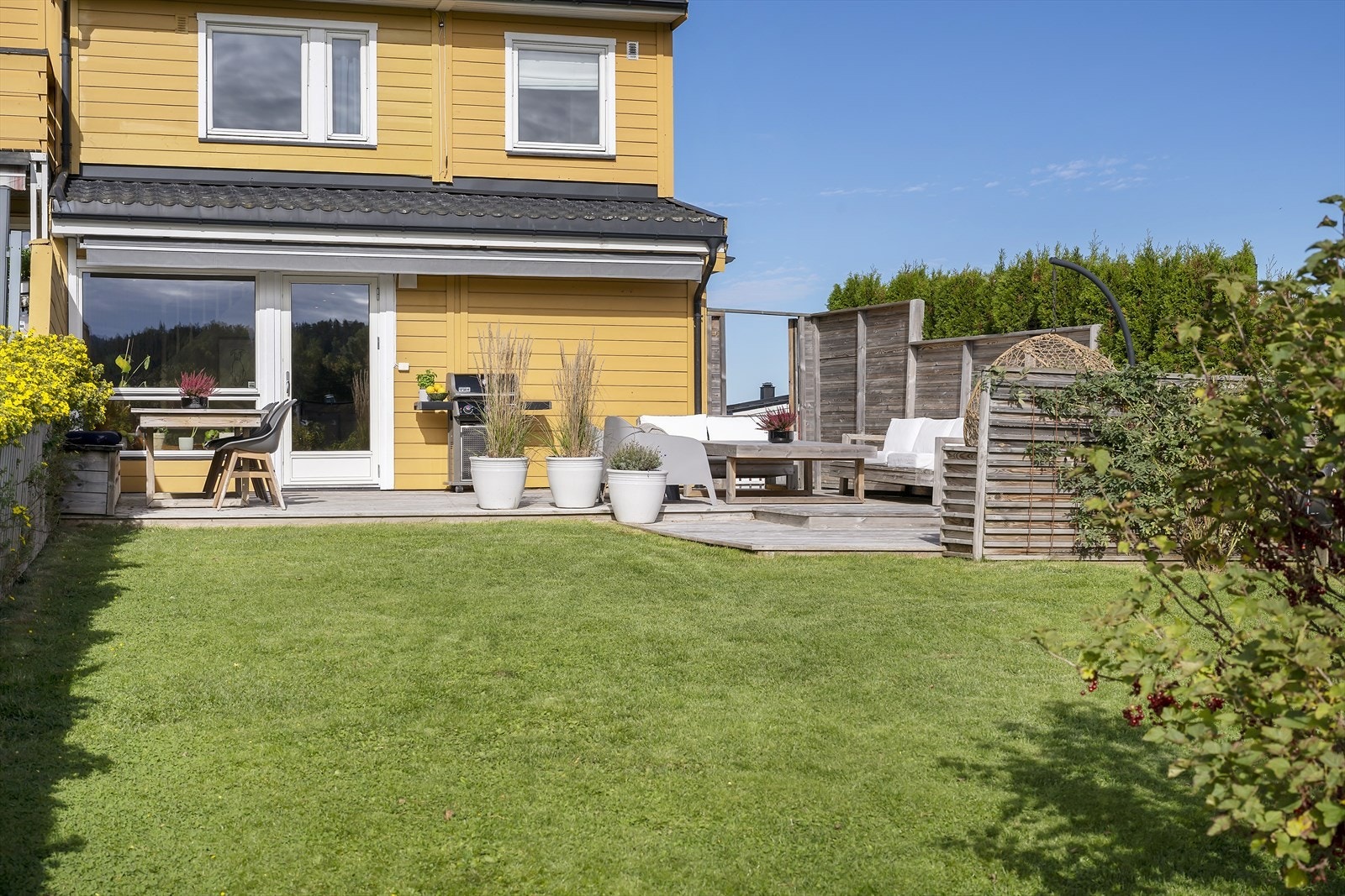 Terrassen går videre ut mot hage med plen og skjermende beplantning. Galleribilde