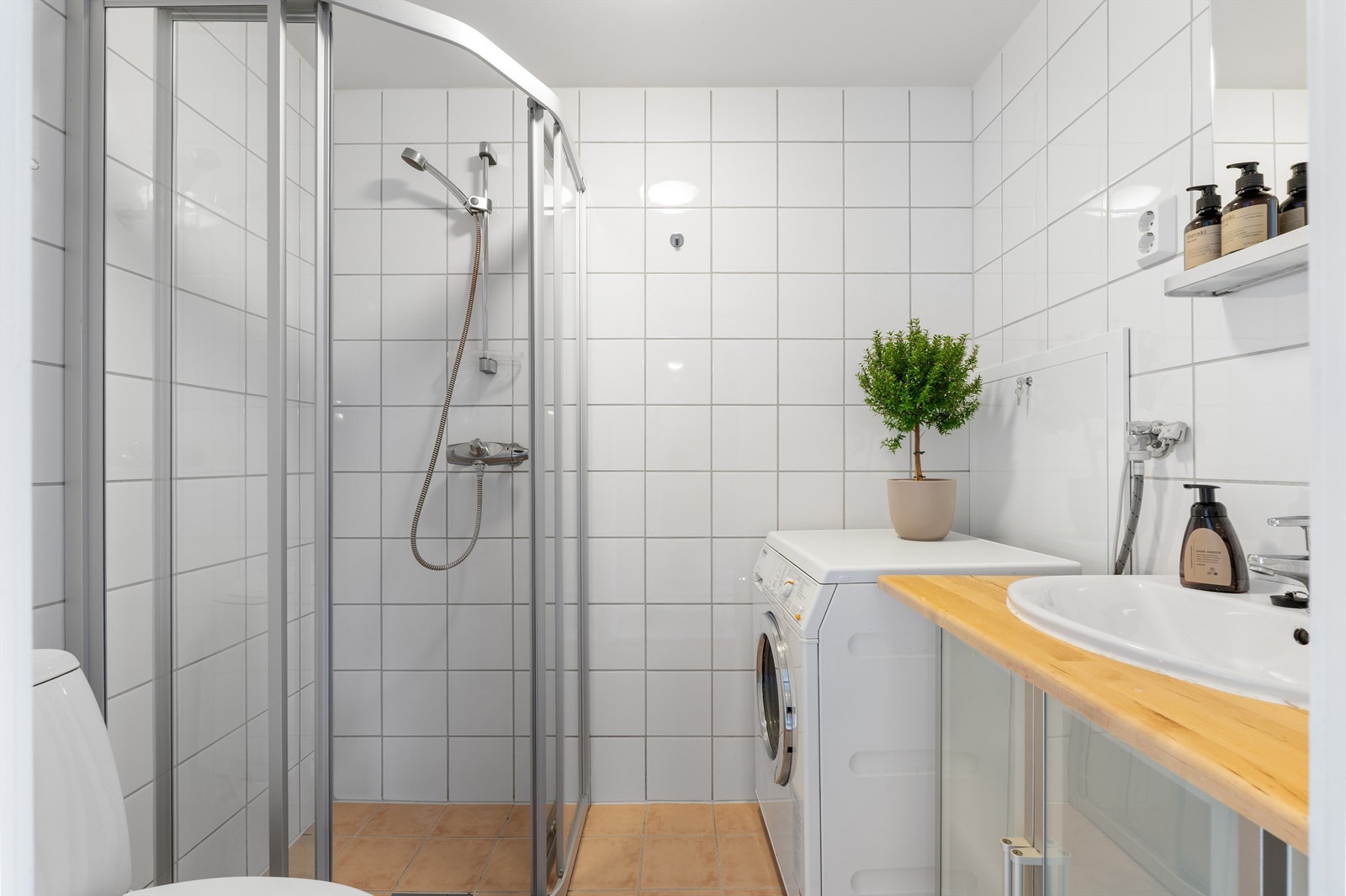 Baderom med flislagte overflater, gulvvarme og opplegg for vaskemaskin. Servantinnredning med overliggende speil og tilhørende hylle. Galleribilde
