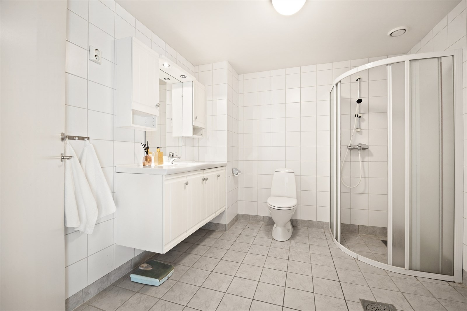 Badet er helfliset med varme i gulvet. Utstyrt med toalett, servant med innredning og speil samt dusjsone. Galleribilde