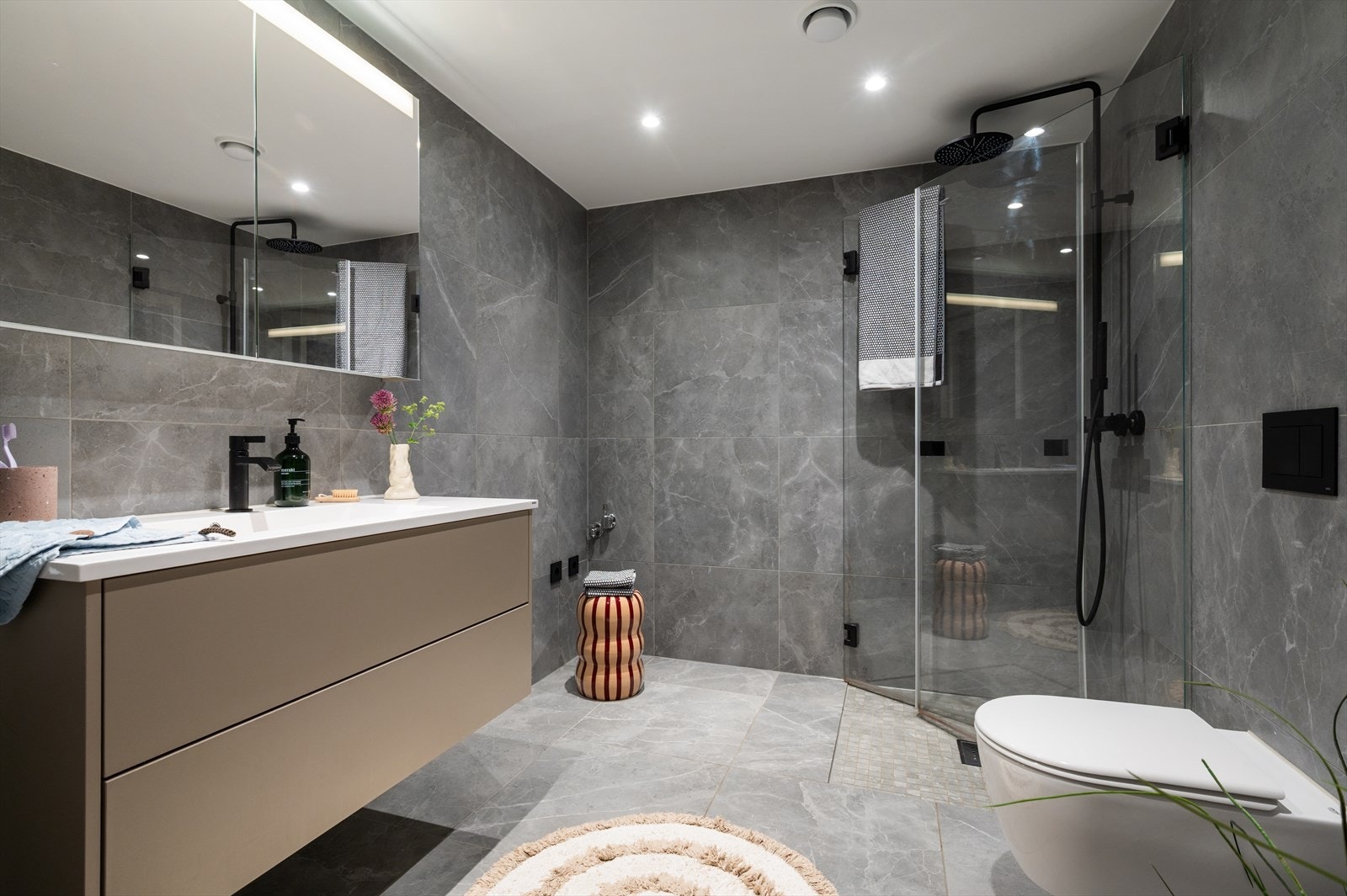 Stort og elegant bad i lune gråtoner, komplettert med stilrene svarte detaljer, malt himling med downlights og behagelig regndusj. Galleribilde