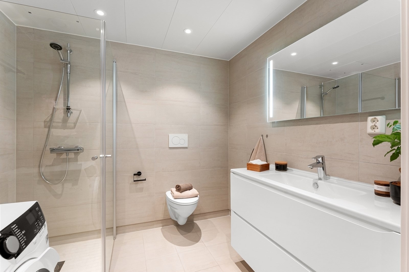 Badet er innredet med servant i skuffeinnredning, speil med integrert belysning, vegghengt toalett, dusj med innfellbare dører og opplegg for vaskemaskin og tørketrommel. Galleribilde