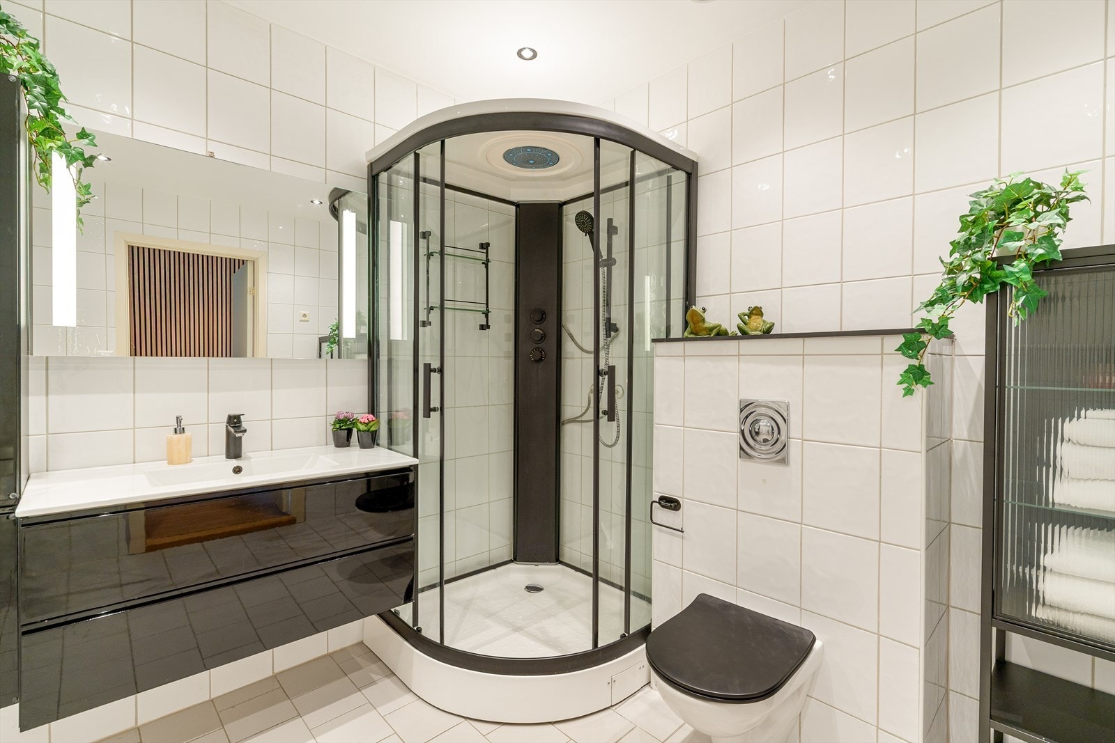 Badet har vegghengt servant, skap og speil, dusjkabinett og vegghengt toalett. Galleribilde