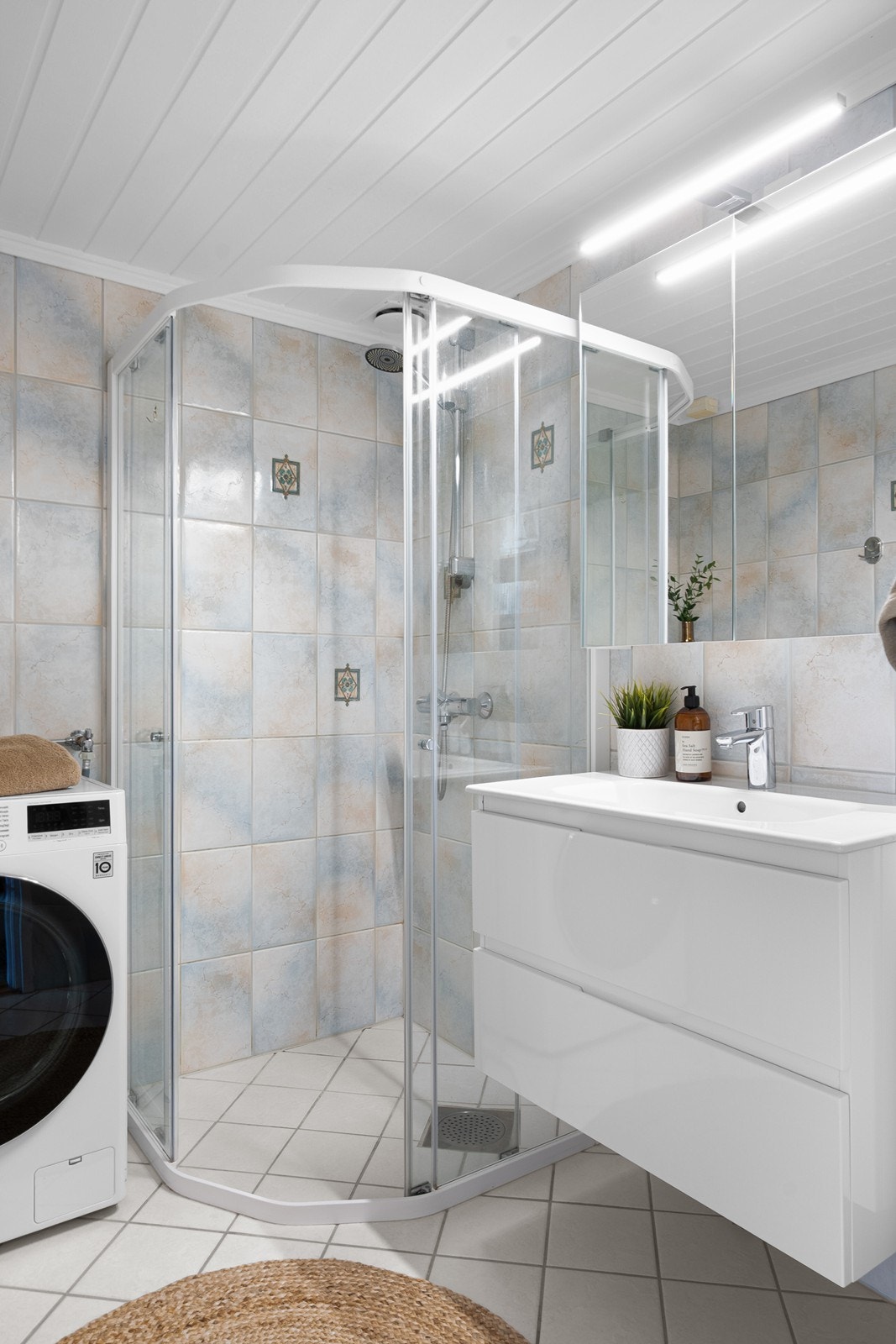 Badet har flislagte overflater og gulvvarme. Innredningen inkluderer servant med skuffer, speil og dusjhjørne med kabinettdører, samt opplegg for vaskemaskin. Galleribilde