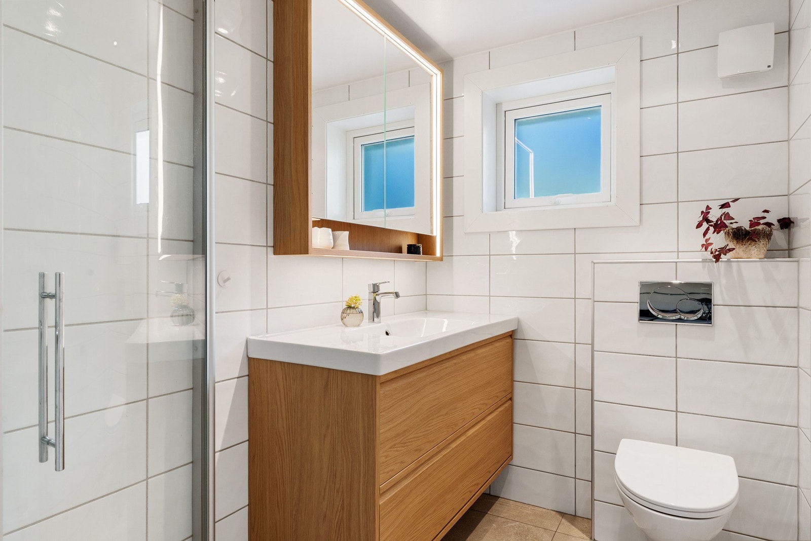 - Badet fremstår lyst og klassisk med flislagte gulv og vegger, dusjhjørne med dusjvegger, vegghengt toalett og moderne baderomsinnredning med servant - Galleribilde