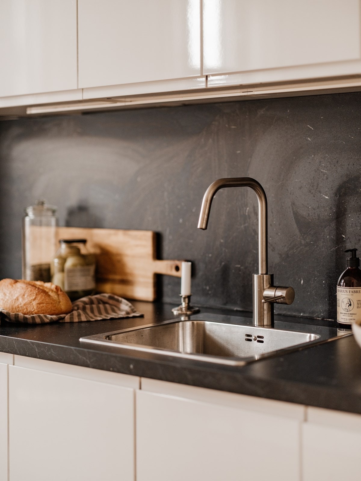 Kjøkkeninnredning fra IKEA med glatte fronter, plater på vegg over benkeskap, laminat benkeplate med nedfelt kum i rustfritt stål og kullfilterventilator. Galleribilde