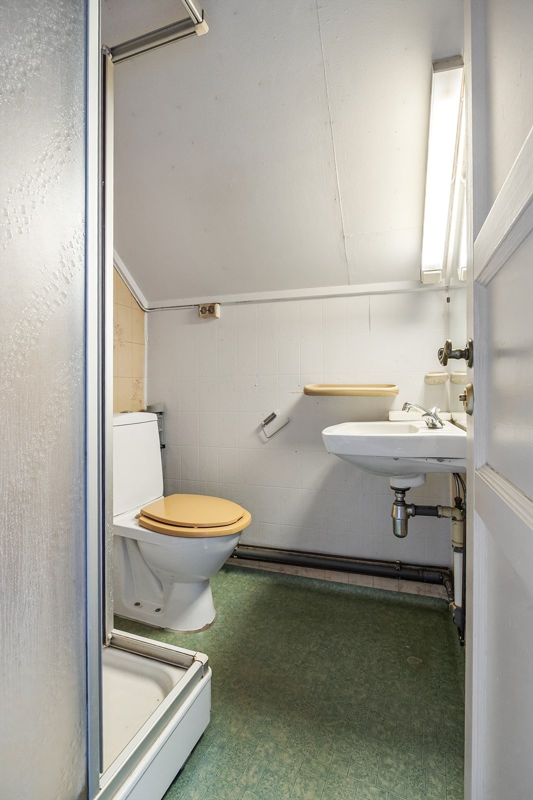 Baderom med vegghengt servant, speil med overlys, dusjkabinett og gulvstående toalett. Gulvbelegg på gulv og tapet på vegger. Galleribilde