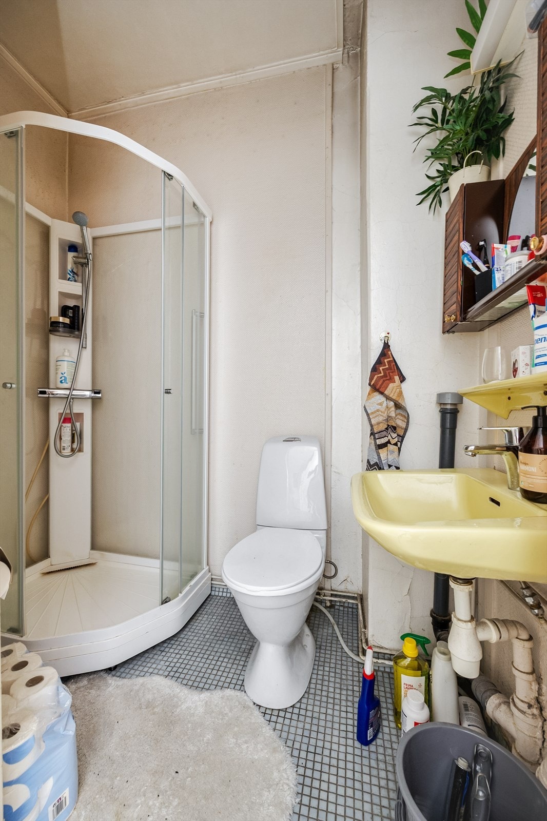 Baderom med fliser på gulv. Badet er innredet med vegghengt servant, speil, dusjkabinett og gulvstående toalett. Galleribilde