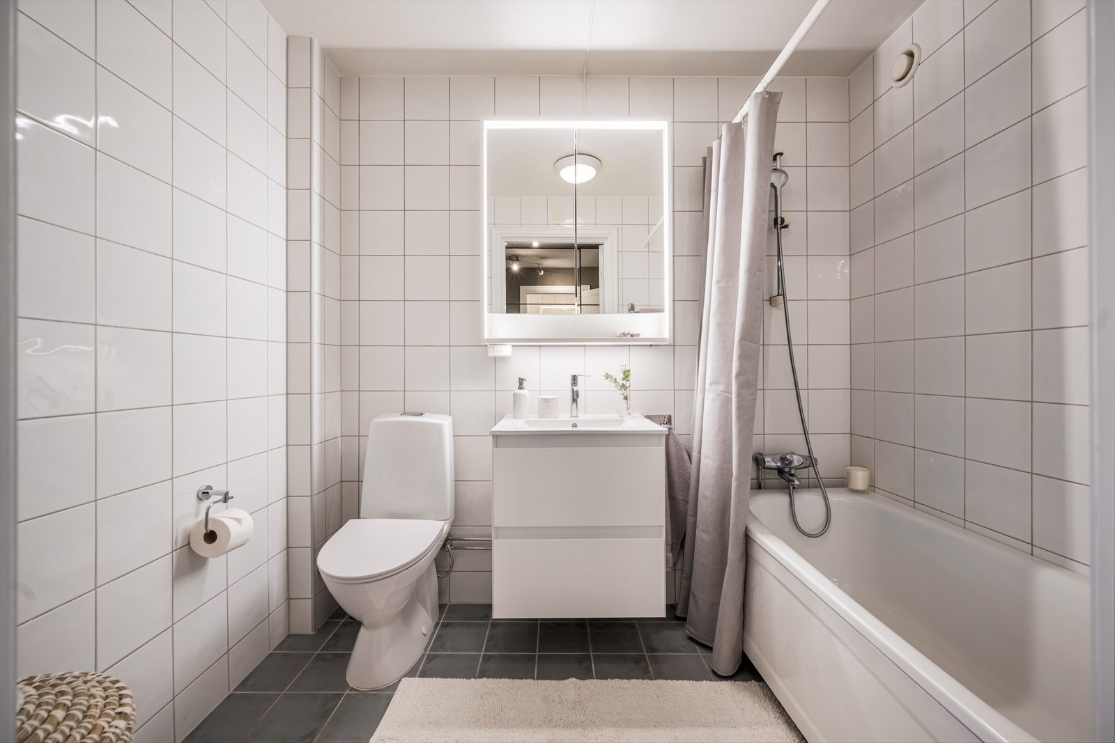 Badet har et klassisk uttrykk med flislagte vegger og gulv - rommet er praktisk innredet med skuffeseksjon og heldekkende, nedfelt servant, ettgreps blandebatteri og speilskap med belysning Galleribilde