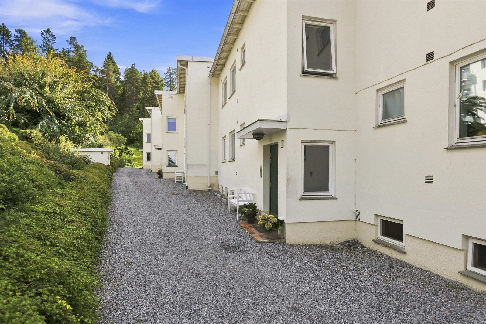 Velholdt fasade med et pent og klassisk uttrykk, omkranset av frodige og grønne utearealer. Galleribilde