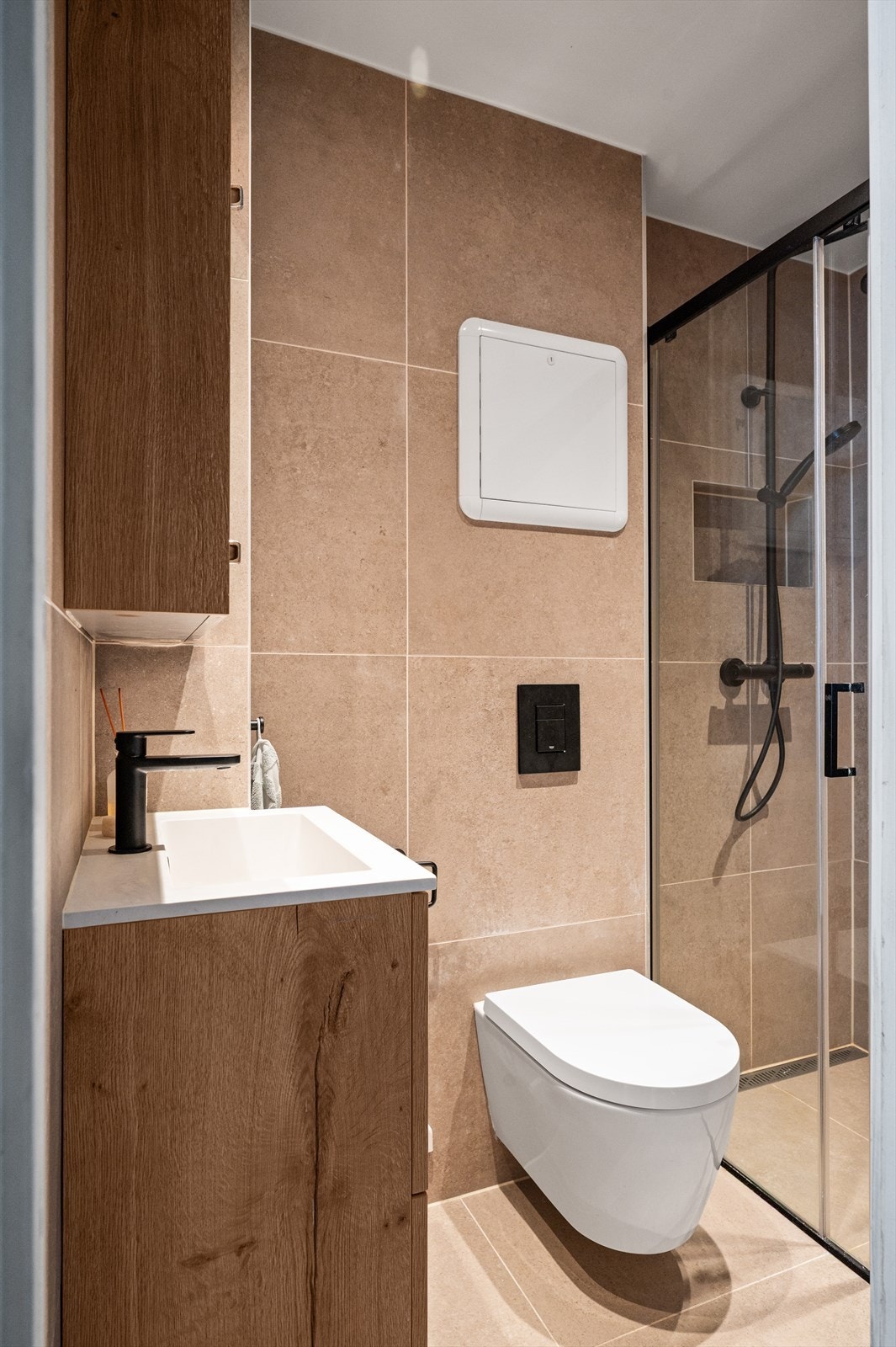 Badet er innredet med servantskap, dusjnisje med glassdører, veggmontert WC og rørfordelingsskap. Galleribilde