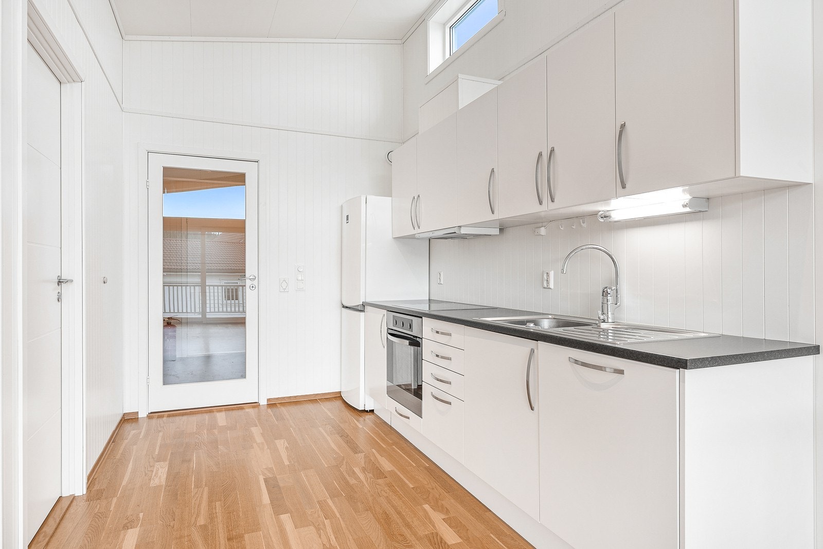 Kjøkkeninnredning med hvite slette fronter og laminat benkeplate. Det er godt med skap- og benkeplass, og har opplegg for hvitevarer. Galleribilde