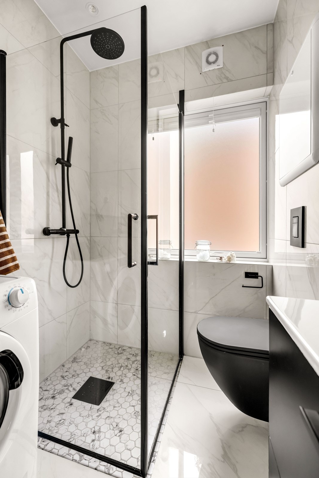 Badet har en gjennomgående stilig finish med detaljer som sort vegghengt toalett og innsvingbare dusjdører i glass med sorte detaljer. Galleribilde