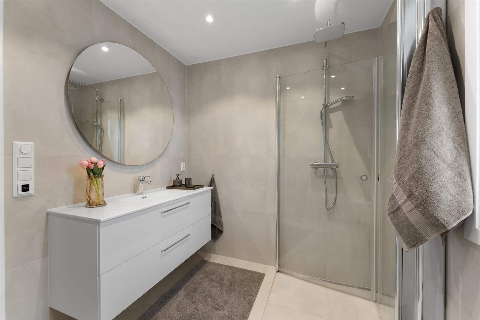 Badet har heldekkende servant med underskap, speil og belysning, samt dusjhjørne med herdet glass og veggmontert toalett med innebygget sisterne. Galleribilde