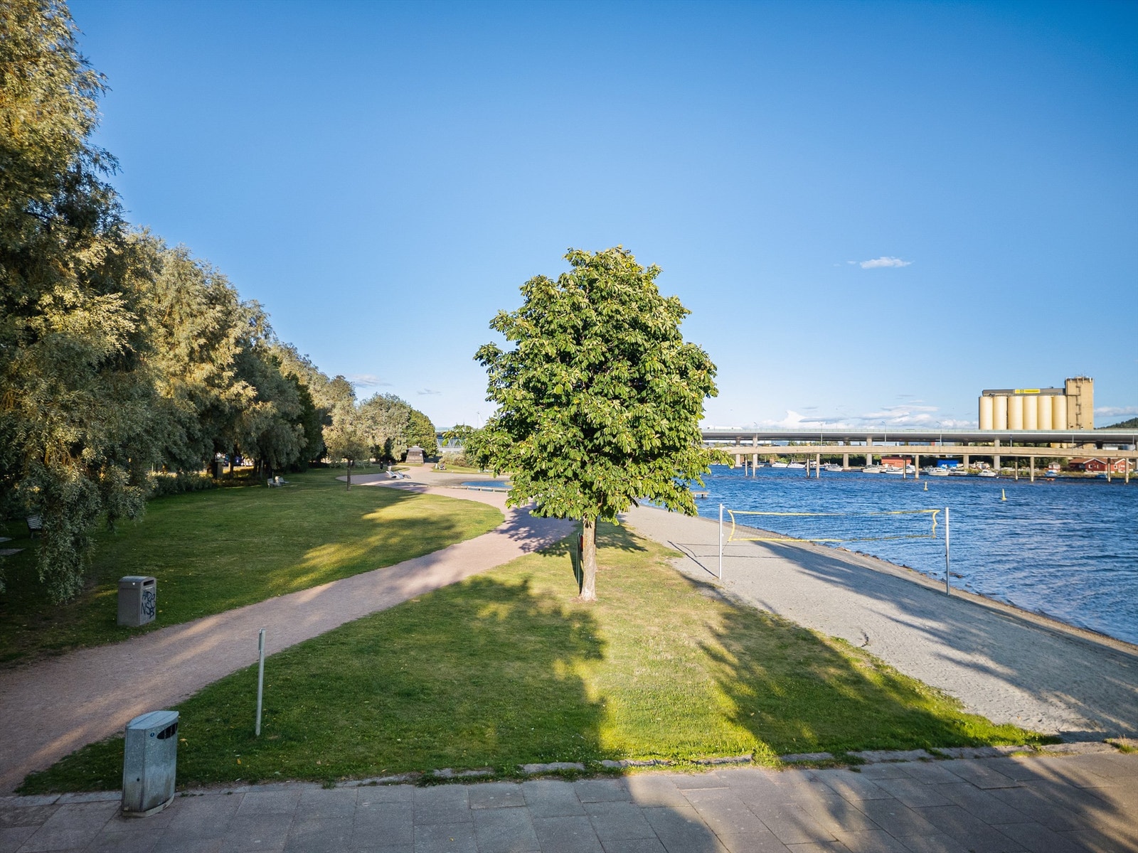 Pent opparbeidet strandpromenade med grøntområder, lekeplasser, volleyballbane og badeplass. Galleribilde