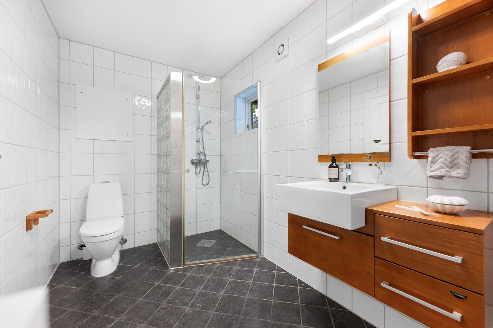 Badet er romslig og har lyse flislagte vegger, og mørke fliser på gulv med elektriske varmekabler. Galleribilde