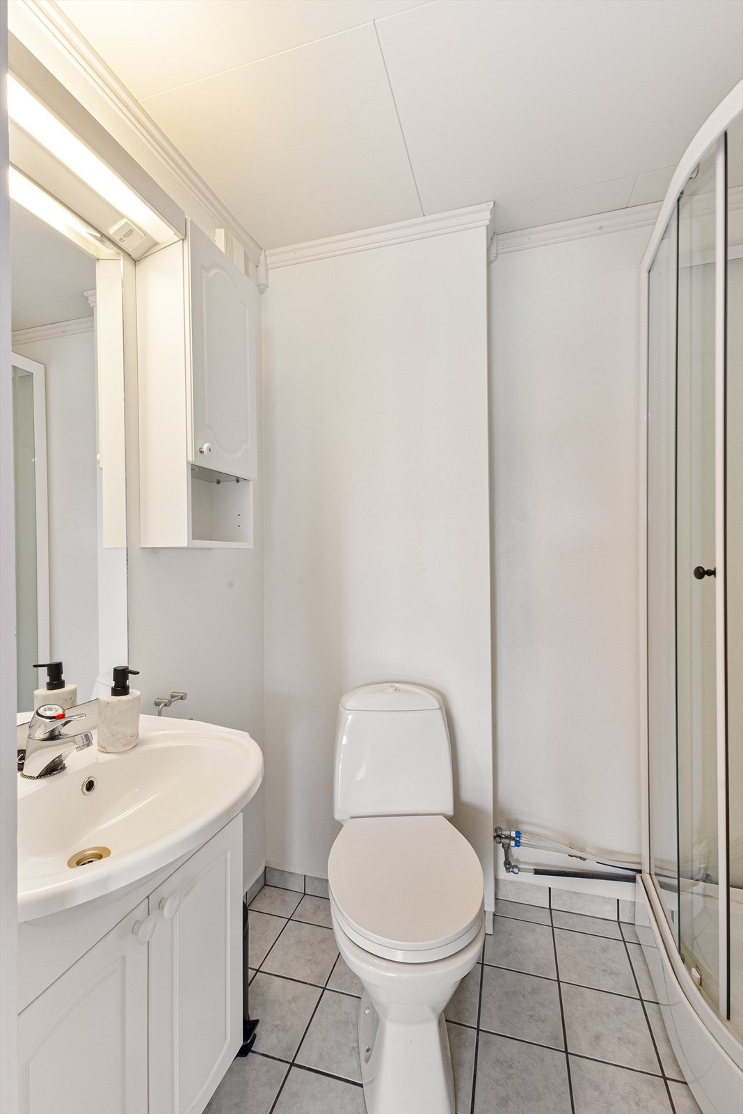 Badet er utstyrt med veggmontert servant og dusjkabinett, samt har flislagt gulv for enkel rengjøring og vedlikehold. Galleribilde