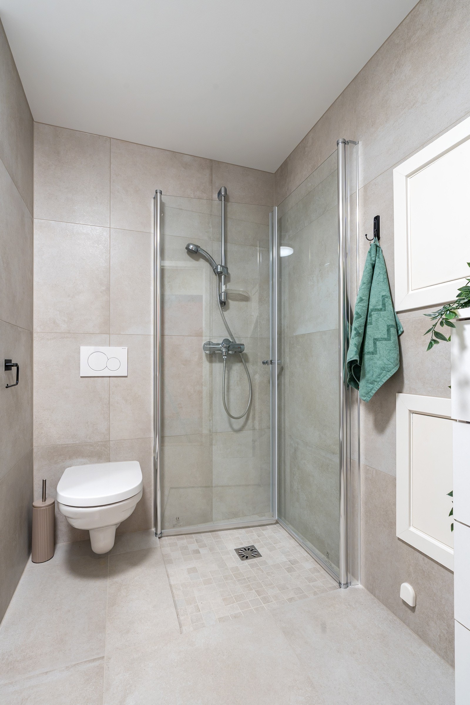 Badet er utstyrt med heldekkende servant, dusjvegger og veggmontert toalett - En praktisk og stilren innredning.