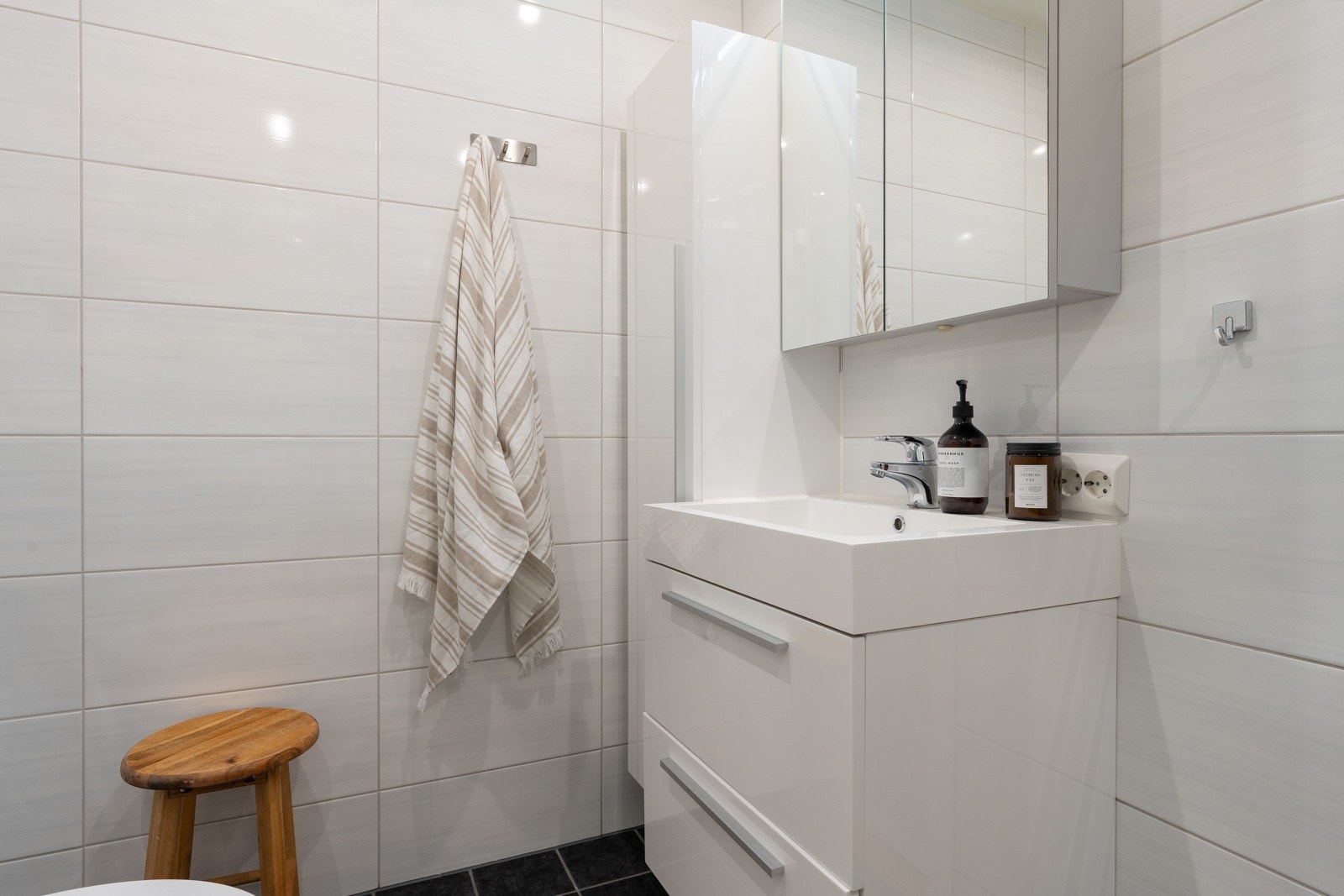 Badet er innredet med dusjkabinett og servant med praktisk oppbevaring.