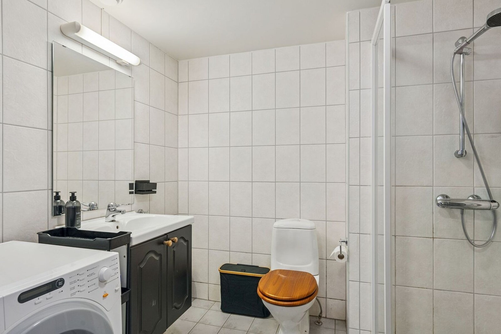 Badet har flislagt overflater med varmekabler i gulvet. Bad har montert klosett, servant, dusj med glassvegg/dør og opplegg til vaskemaskin. Baderomsinnredningen er malt i samme farge som kjøkkenet, og gir leiligheten et fint og helhetlig inntrykk Galleribilde