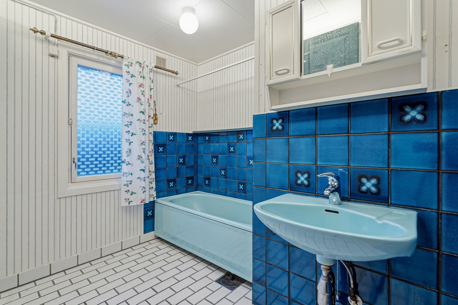 Badet fremstår som romslig og funksjonelt, med en særegen og tidløs stil. Flislagt gulv gir et slitesterkt og praktisk underlag, mens vegger med fliser og panel skaper en spennende kontrast og et retroinspirert uttrykk. Galleribilde