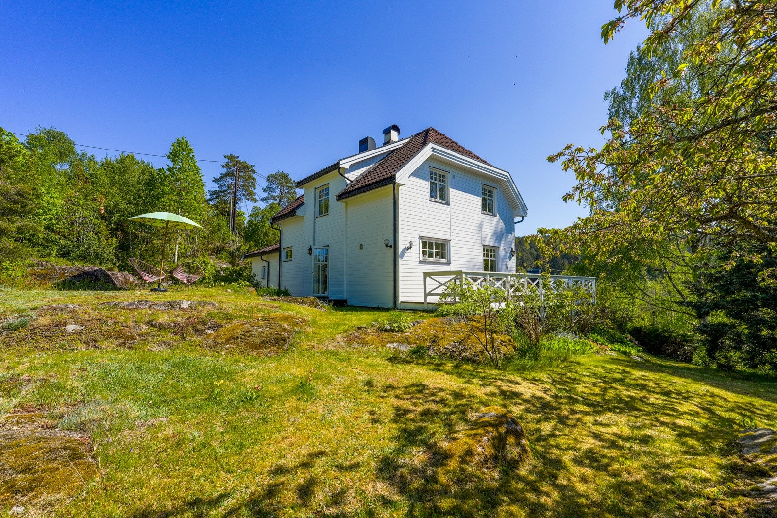 Tomten er pent opparbeidet med flere prydtrær og busker, ulike blomsterbed, hekker og gruslagt gårdsplass med plass til flere biler. Galleribilde