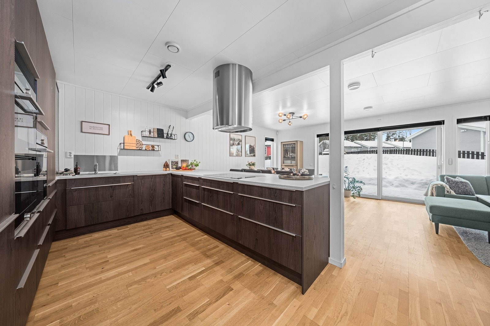 Kjøkkenet har parkett på gulv og lyse panelplater på vegger, noe som gir et moderne og innbydende uttrykk. Norema-kjøkken med glatte fronter og en praktisk kjøkkenøy som åpner rommet mot spisestuen. Galleribilde