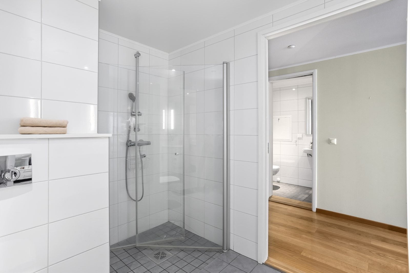 I den romslige dusjen (ca. 1 x 1 meter), er det lagt matchende fliser av mindre dimensjon enn øvrige gulvfliser og dusjvegger med glassdører av herdet glass. Legg også merke til detaljen med nedsenket gulv i dusjsonen og dusjløsningen. Galleribilde