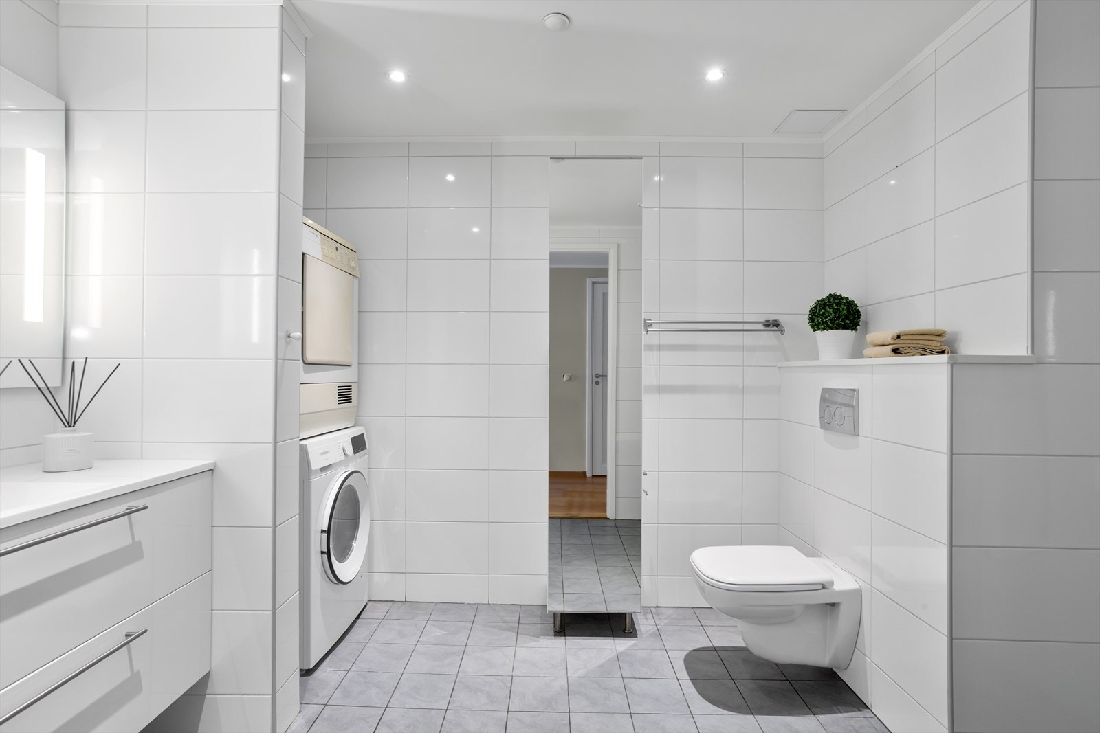 Hovedbadet er utstyrt med dusj, toalett og rommet har flislagte vegger og flislagte gulv med elektrisk gulvvarme. Veggene har tidsriktige, rektangulære veggfliser mens det på gulvet er valgt en gråtonet farge for å skape en matchende kontrast. Galleribilde