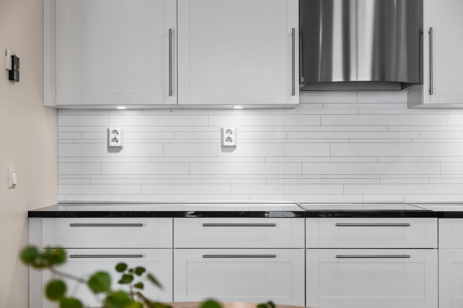 Stiltilpasset ventilator fra Røråshetta med oval front i børstet stål. Utstrakt bruk av underskap med praktiske kolonialskuffer. Innfelte LED-lys med nivåjustering fra fjernkontroll i de av overskapene som har glassdører. Galleribilde