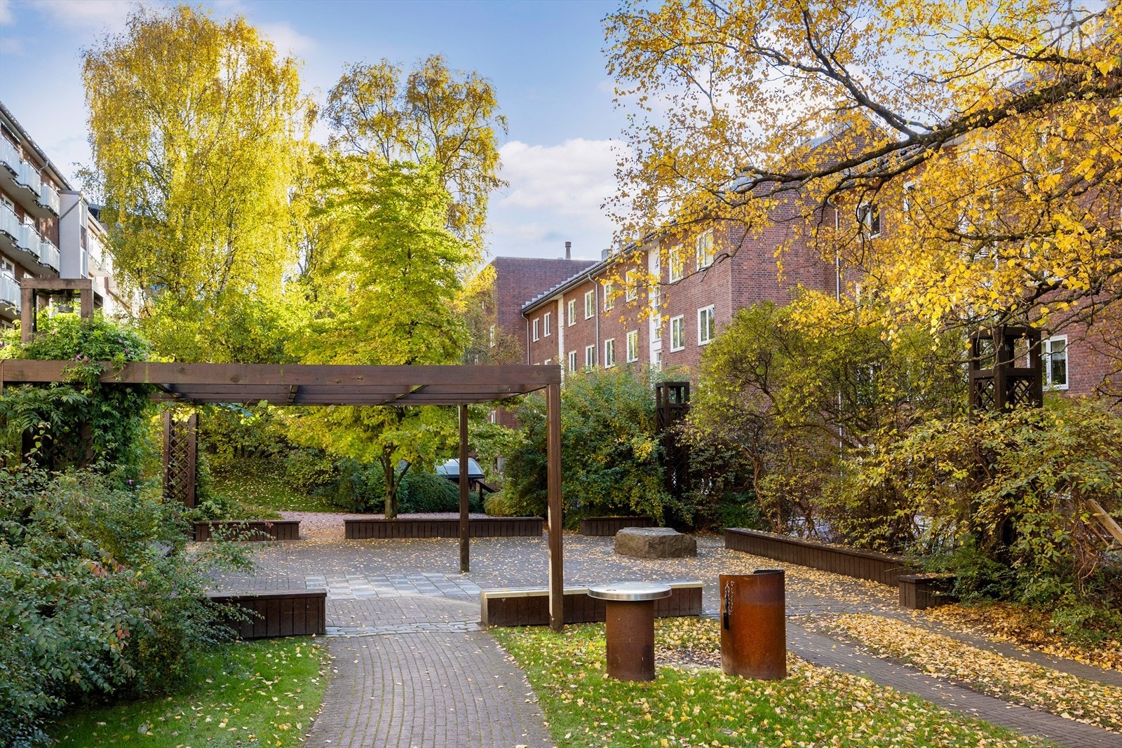 Borettslagets store, velstelte og frodige bakhage - et skjermet felles uterom med flere sittegrupper og hyggelige oppholdsplasser. På sommerhalvåret rigges det gjerne til med grill og solstoler, perfekt for lange, solrike dager i grønne omgivelser. Galleribilde